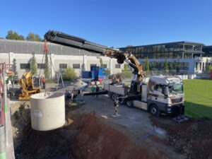 Versetzen der Regenspeicher vom Kran des Lieferfahrzeugs in die vorbereitete Baugrube. Fünf Betonbehälter, die untereinander verbunden sind, bilden die so genannte Mehrbehälteranlage, der ein Filterschacht vorgeschaltet wurde. Dieser reinigt das vom Dach kommende Regenwasser. Foto: Carderie KG 